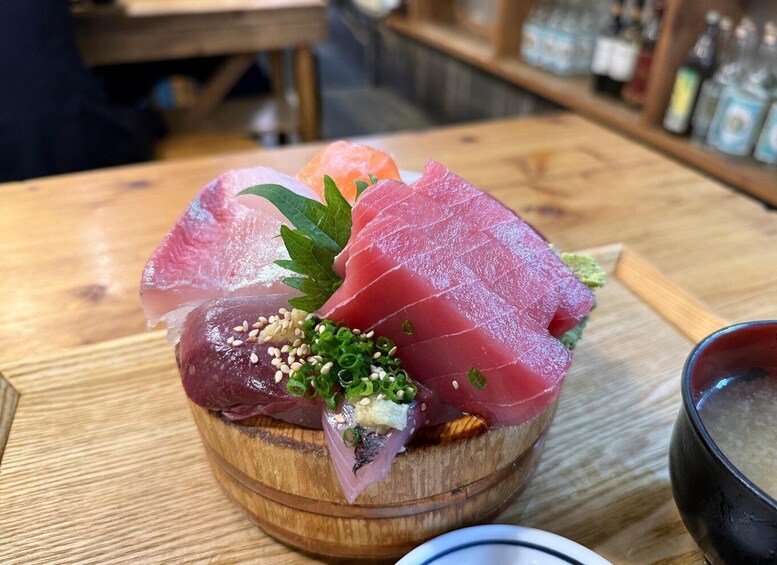 A wooden table with a wooden bowl containing various sashimi pieces, garnished with green onions and sesame seeds. 5