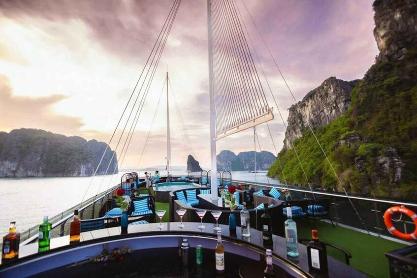 A boat deck with lounge chairs, bar area, and a view of the sea and cliffs. 1