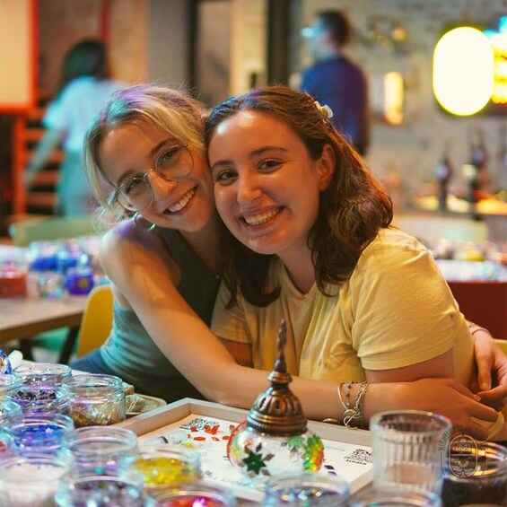 Dos personas sentadas en una mesa con varios recipientes de vidrio y un adorno. 4