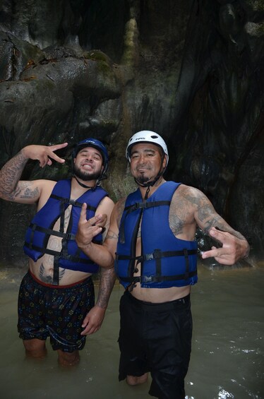Two people in blue life vests posing in a cave with water. 2
