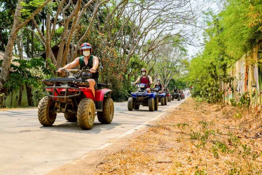 People riding atv's on a road surrounded by trees. 5