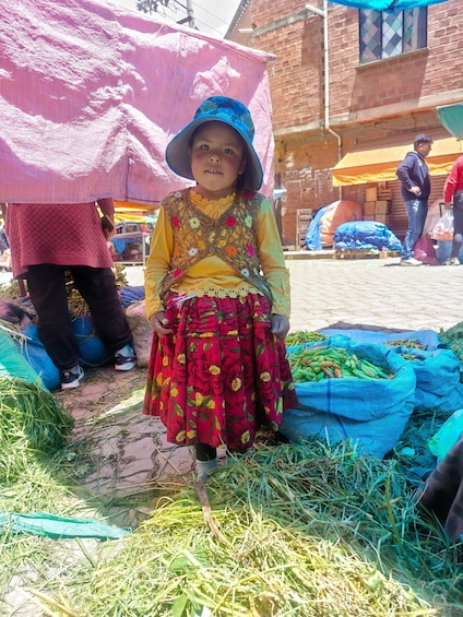 A child in a colorful outfit standing among sacks of produce at a market. 1