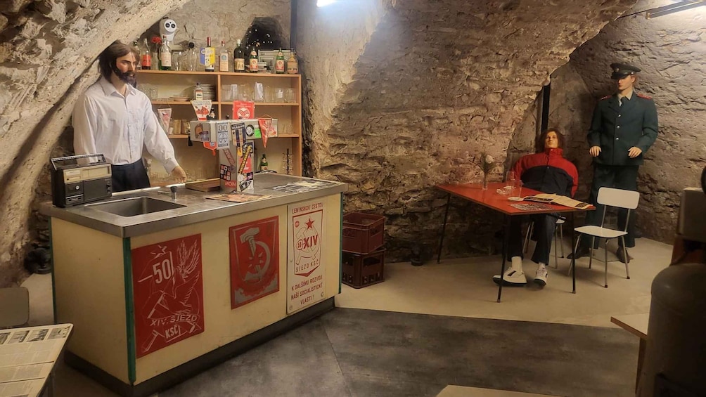 A room with a bar area, a person standing behind the bar, and another person seated at a table. 5