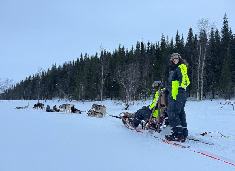 A snowy landscape with a group of huskies pulling a sled, and a person standing on skis. 2
