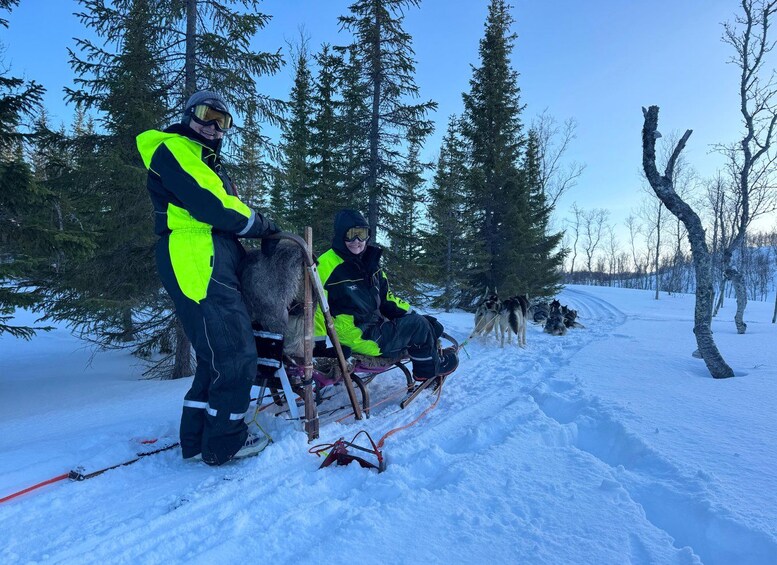 Two people in bright clothing sitting on a sled with a dog in a snowy forest. 3