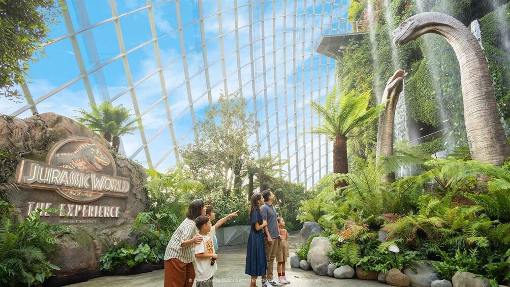 A Jurassic World attraction entrance with a large dinosaur sculpture and lush greenery. 1