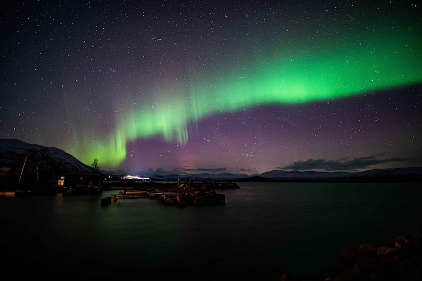 The Northern Lights over a calm lake with a dock and buildings in the foreground. 5