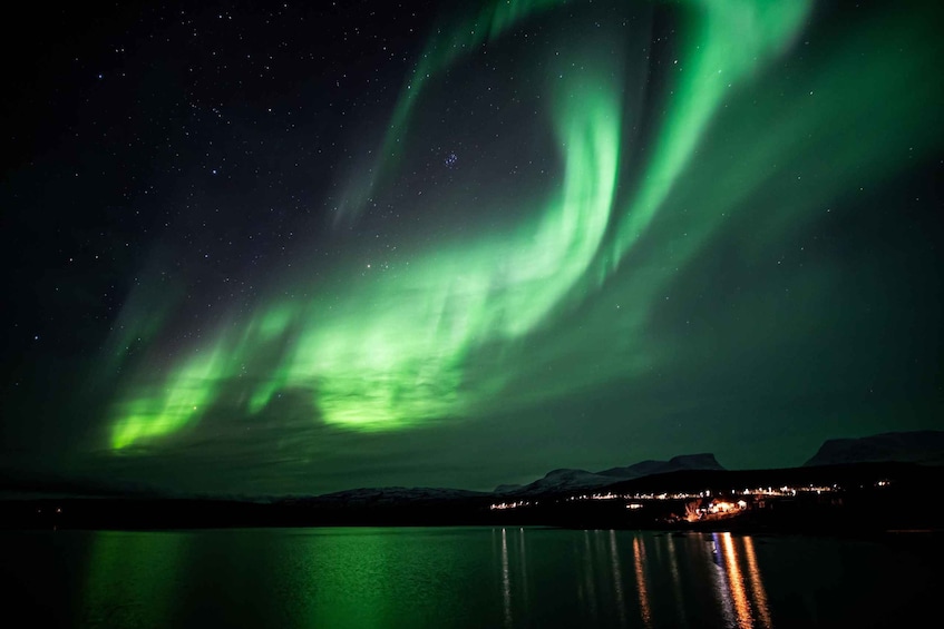 The Northern Lights over a calm lake with a town in the distance. 4