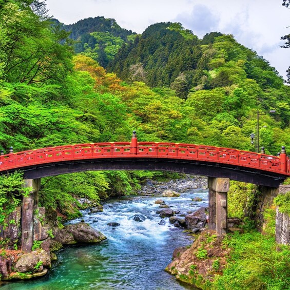 A red bridge over a flowing river surrounded by lush greenery and hills. 1