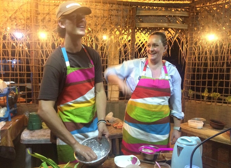 Two people in a kitchen, wearing colorful aprons, preparing food. 1