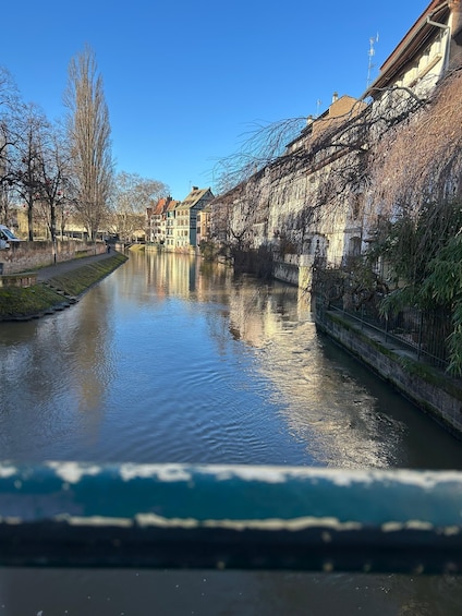 A calm river with buildings on one side and leafless trees on the other. 2