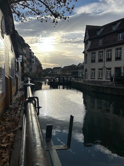A canal with buildings on either side, a bridge in the distance, and a partly cloudy sky. 1