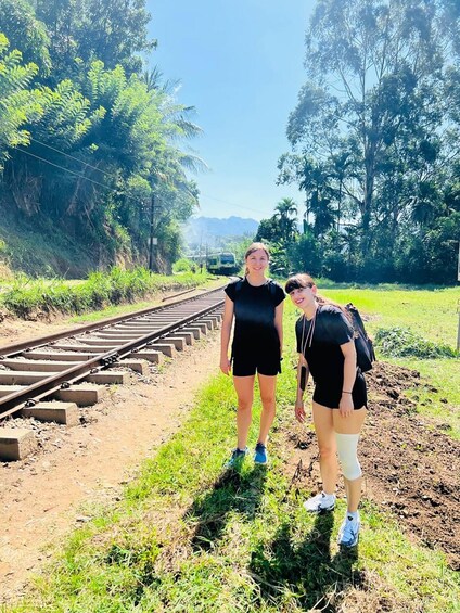 Two people standing on a railway track with greenery and trees in the background. 5