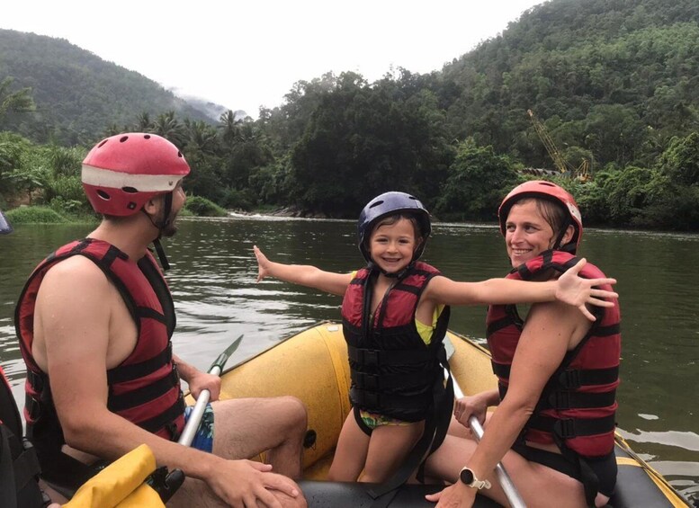 Three people in a yellow raft on a river surrounded by forested hills. 3