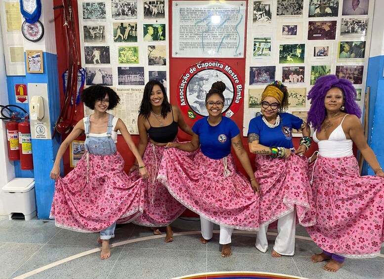 A group of women in traditional attire with a banner in the background. 2