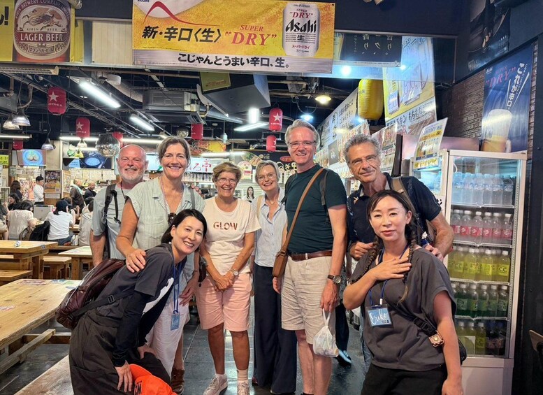 A group of people posing in a busy indoor market with various food stalls and beverage signs. 4