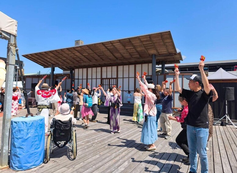 A group of people performing a traditional dance on a wooden deck with a covered area in the background. 5