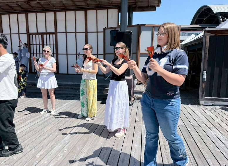 A group of people on a wooden deck holding objects, with a building in the background. 3