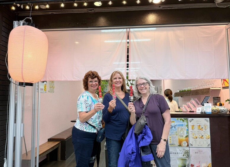 Three people standing in front of a shop with a signboard and a hanging paper lantern. 3
