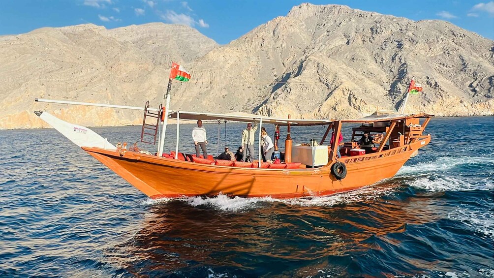 A wooden boat with two flags on a calm sea with rocky mountains in the background. 1