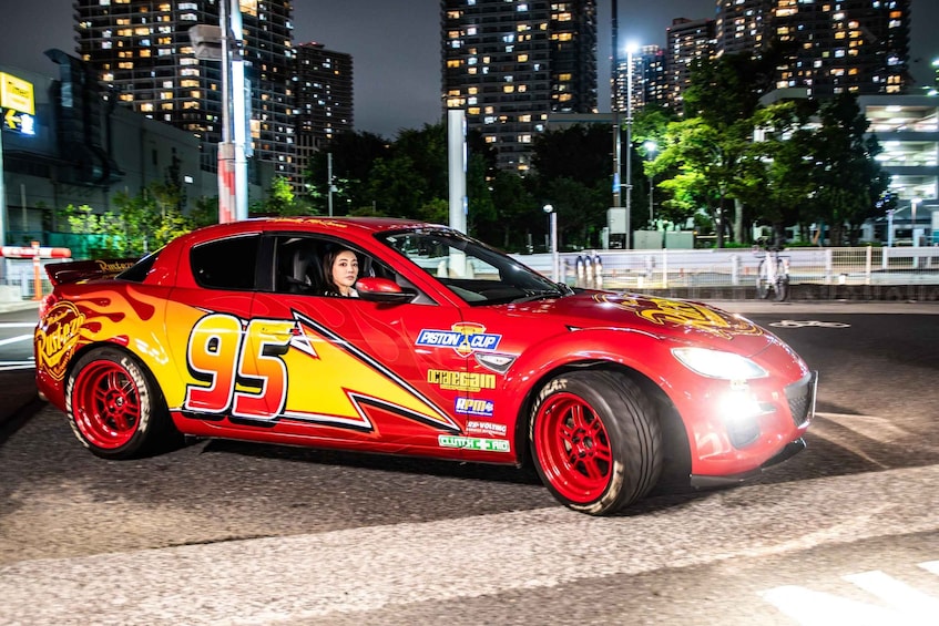 A red sports car with racing decals parked on a city street at night. 3