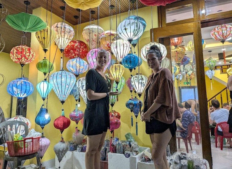Two people standing in front of a wall of colorful lanterns. 1