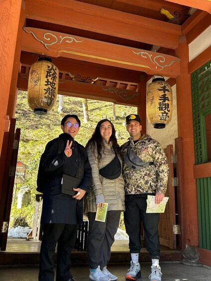 Three people standing in front of a traditional wooden structure with hanging lanterns. 5