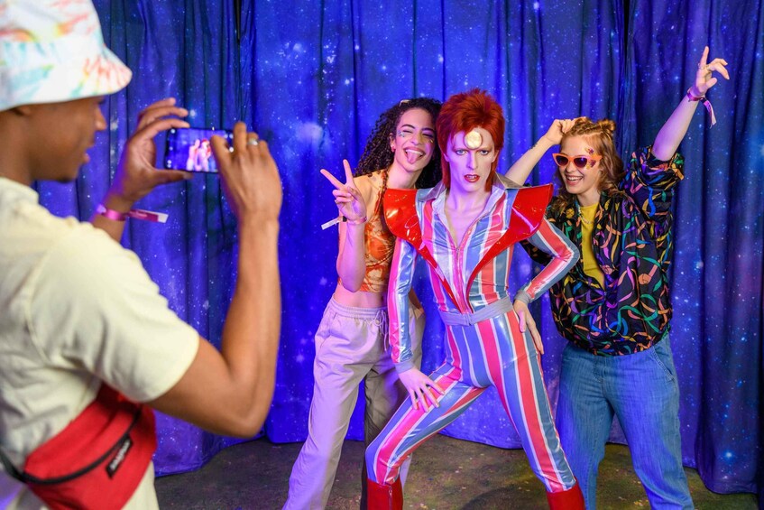 A person taking a photo of three people in colorful outfits against a blue curtain backdrop. 3