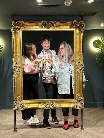 Three people standing in front of a large ornate golden-framed mirror. 5