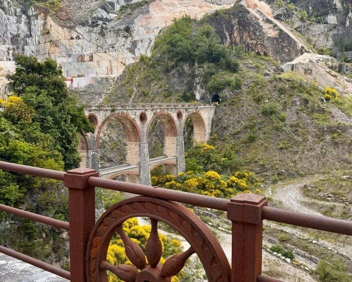 A stone bridge with arches over a valley, surrounded by rocky terrain and greenery. 1