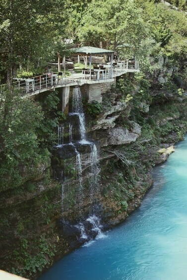 A waterfall cascading down a cliff into a river, with a wooden bridge and gazebo above. 3
