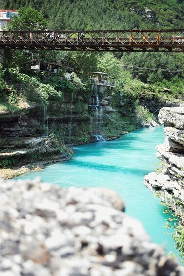 A turquoise river flowing through a rocky gorge, a bridge overhead, and a small wooden structure on the left bank. 2