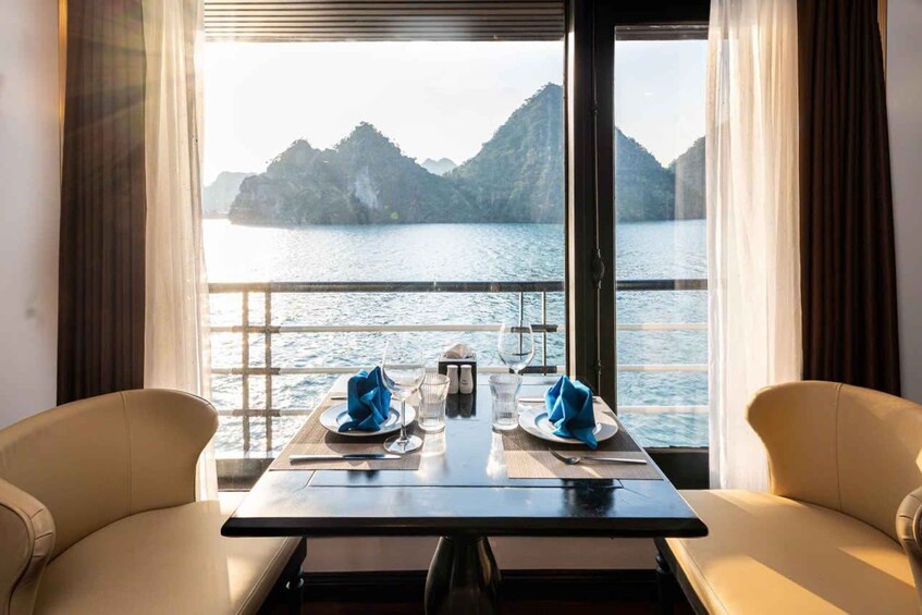 A dining table with two chairs, set for two, overlooking a body of water with mountains in the background. 1