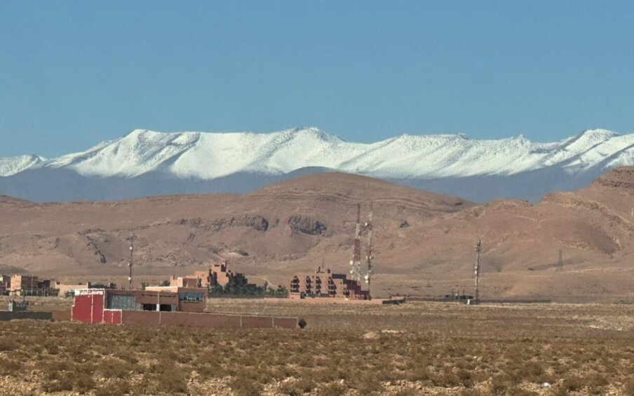 A desert landscape with a small settlement and snow-capped mountains in the background. 1