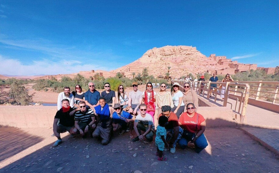 A group of people posing in front of a large, reddish-brown rock formation with a clear blue sky in the background. 4