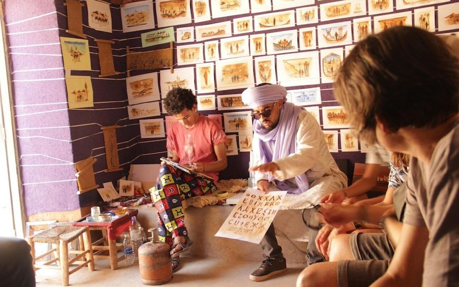 A group of people sitting on the floor, surrounded by a wall of framed drawings. 3