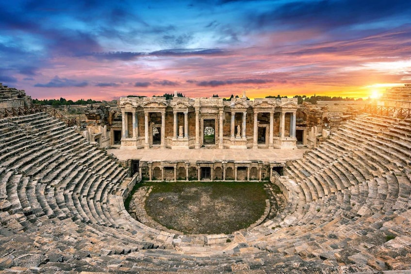 An ancient amphitheater with stone steps and a central stage, surrounded by ruins. 5
