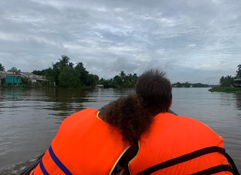 A person in an orange life jacket paddling a boat on a river. 1