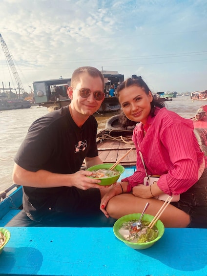 Two people sitting on a boat, holding bowls of food. 3