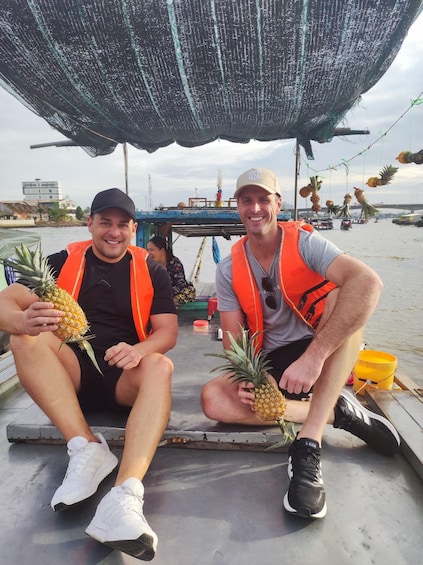 Two people on a boat holding pineapples. 2