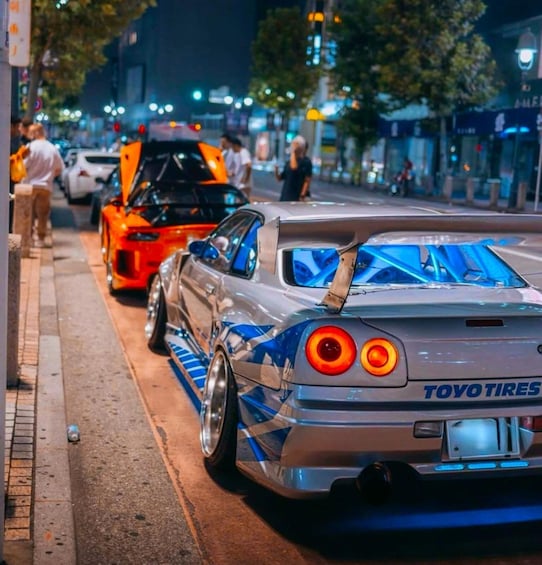 A silver sports car with blue accents parked on a city street at night. 1