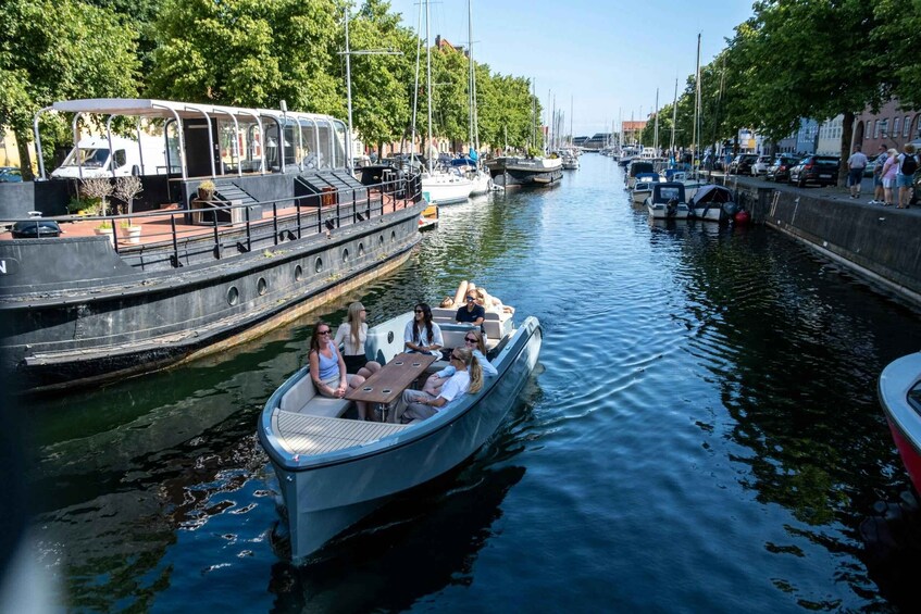 A narrow canal with boats, a covered boat, and a row of trees along the banks. 3