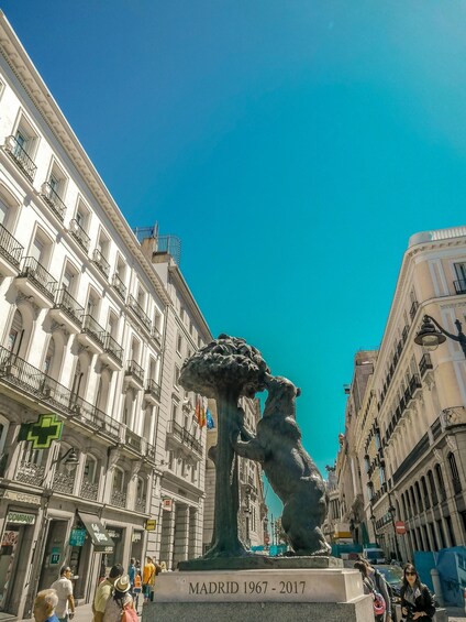 A sculpture of a tree with a figure in a hat, surrounded by historic buildings. 2