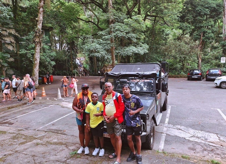 A group of people posing in front of a vehicle in a parking area surrounded by trees. 5