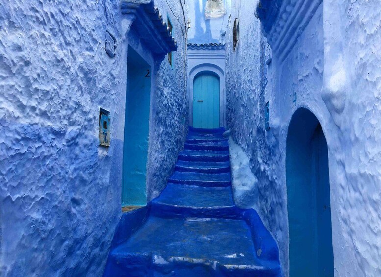 A narrow alleyway with blue-painted walls and steps leading to a door. 3