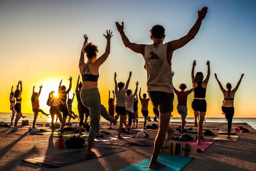 A group of people doing yoga on mats at sunset by the beach. 5