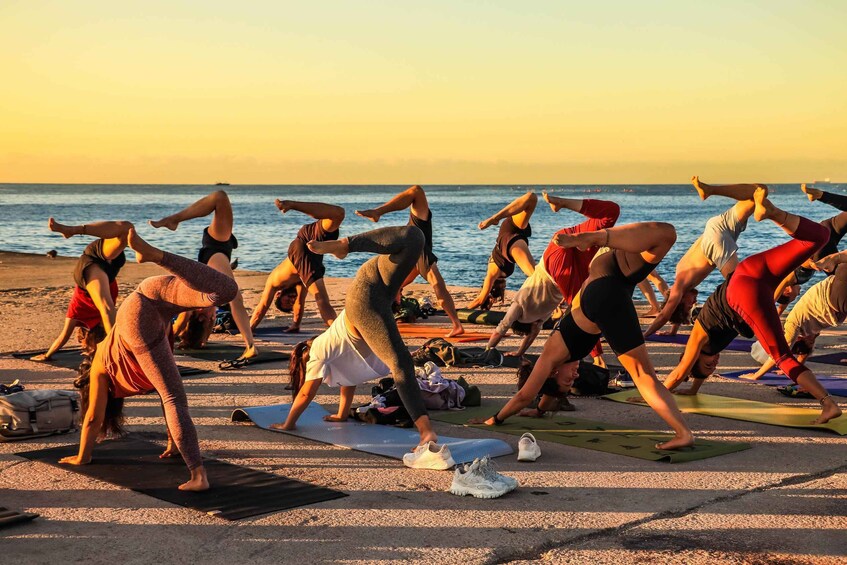 A group of people doing yoga on mats by the beach at sunset. 2