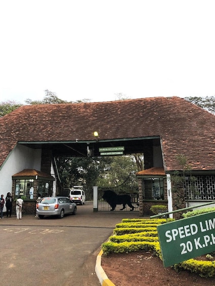 A building with a sign reading "Nairobi National Park Main Gate Entrance" and a speed limit sign indicating 20 K.P.H. 4