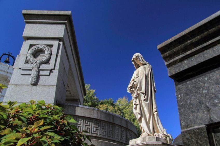 Une statue représentant une figure drapée, un monument en pierre orné de motifs de serpent et un ciel d’un bleu limpide. 5