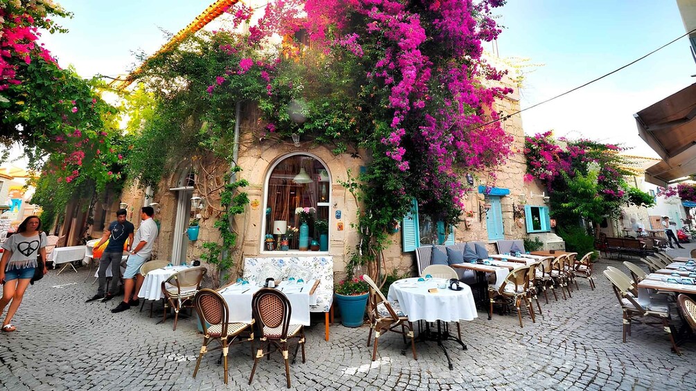 A charming outdoor café with tables and chairs, surrounded by vibrant bougainvillea flowers and rustic stone walls. 2